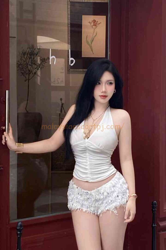 Vietnamese escort Yumi wearing white halter top and shorts posing outside a door